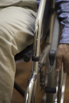 Man sitting in shiny steel metal wheel chair wearing blue shirt pushing wheel to move himself forward in hospital clinic. Color digital photo in warm tones shot from in front with shallow depth of focus.