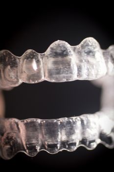 Close up macro photo of invisible transparent plastic dental brackets set against black studio background. Artistic color digital photo with shallow depth of focus.