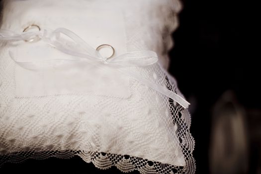Color artistic digital rectangular horizontal photo of the two wedding rings tied with bows to a lace cushion before the marriage ceremony in Madrid Spain. Shallow depth of focus with background defocused. 
