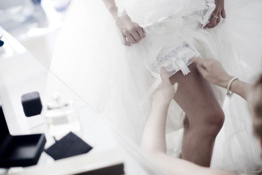 Color artistic digital rectangular horizontal photo of bride putting on wedding bridal garter belt underwear lingerie. Shallow depth of focus with background defocused. 