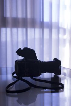 Medium format old vintage analog film camera, viewer, 120 film back, lens and leather strap in silhouette in room on table.