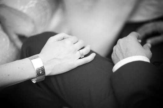 Black and white artistic digital photo of bridegroom in dark suit and white shirt in wedding marriage holding hands with the bride in white long wedding bridal dress. Shallow depth of with background out of focus. 