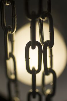 Steel metal chain links silhouette close-up at night in light circle. 