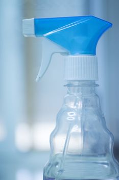 Household domestic cleaning liquid spray plastic bottle in blue and white with plain defocused kitchen house background. 