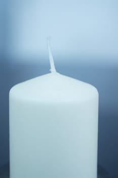 White Candle on plain blue studio background with shallow depth of focus. 