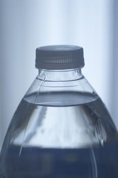 Isolated blue plastic water bottle on a plain blue studio background close-up photo.