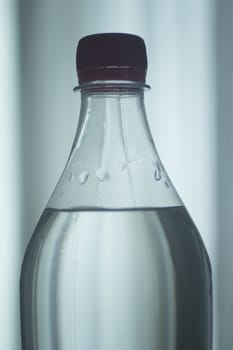 Isolated blue plastic soda lemonade soft drink bottle on a plain blue studio background close-up photo.