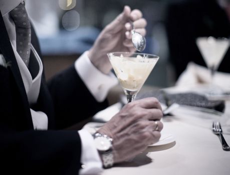Color artistic digital rectangular horizontal photo of hand of man in dark suit and white shirt wedding reception banquet marriage party eating sorbet ice cream dessert from cocktail glass in Barcelona Spain. Shallow depth of with background out of focus. 