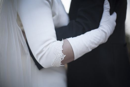 Color artistic digital photo of bridegroom in dark suit and white shirt in church religious wedding marriage ceremony holding hands with the bride in white long wedding bridal dress. Shallow depth of with background out of focus. 