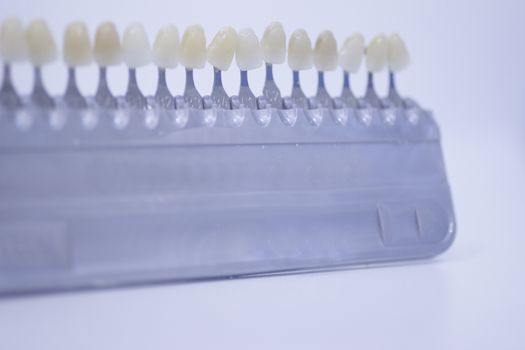 Dentist's tooth color guide used to choose the appropriate natural colors for a patient's tooth implants and crowns on plain white pastel light blue background of the dental surgery clinic table. Close-up macro photo. 