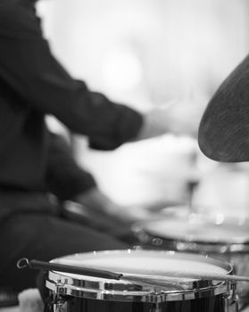 Black and white artistic digital rectangular vertical photo of drumsticks on drum and drummer playing drumset in wedding party reception in Barcelona Spain. Shallow depth of with background out of focus. 