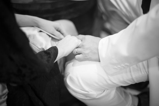 Black and white artistic digital photo of bridegroom in dark suit and white shirt in wedding marriage holding hands with the bride in white long wedding bridal dress. Shallow depth of with background out of focus. 