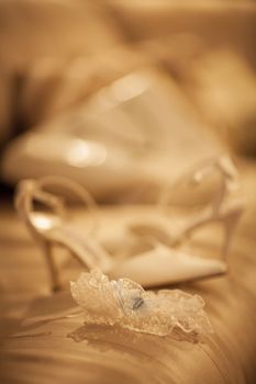 Bridal garter belt lingerie underwear and white wedding shoe of bride on bed photo in gold warm tones. 