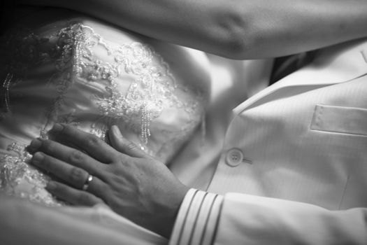 Black and white artistic digital photo of bridegroom in dark suit in wedding marriage event holding hands with the bride in white long wedding bridal dress. Shallow depth of with background out of focus. 