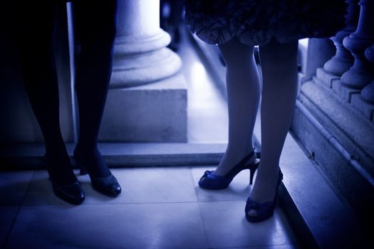 Legs of young ladies wearing high heels shoes and short cocktail dresses standing on shiny tile floor in social event wedding party in Madrid Spain. Blue evening tone color photograph. 