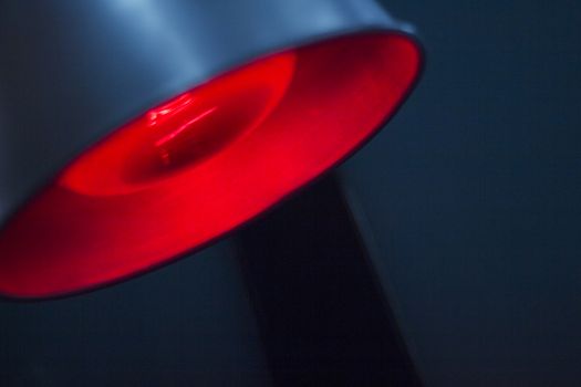 Closeup color digital photo of the bulb of red physiotherapy heat medical rehabilitation lamp in hospital clinic in artistic blue tones. 