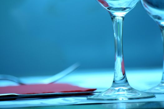 Color close-up photo of a of a wine glass, water glass, knife, fork, and red napkin serviette on a dining table in the restaurant of a nightclub bar at night in Chueca in Madrid Spain. 