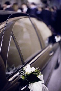 Bridal white flower bouquet on wedding car door with focus on foreground and shallow depth of focus.