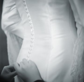 Bride gets help dressing white wedding dress black and white photo.

