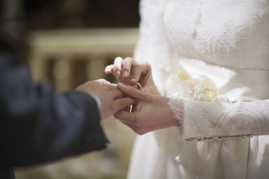 Color artistic digital photo of bridegroom in dark suit and white shirt with cufflinks in church religious wedding marriage ceremony holding hands with the bride in white wedding bridal dress. Shallow depth of with background out of focus. 