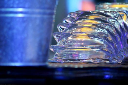 Color photo of a group of upturned clear glass cigarette ash trays sparkling in the light next to a metal ice bucket in a pub / public house restaurant bar at night in Chueca in Madrid Spain. The multiple ashtrays have just been washed and dried, and are displayed upside-down on the top of the bar where they are reflecting the light from above, ready to be filled put on the table for the evening's customers. 