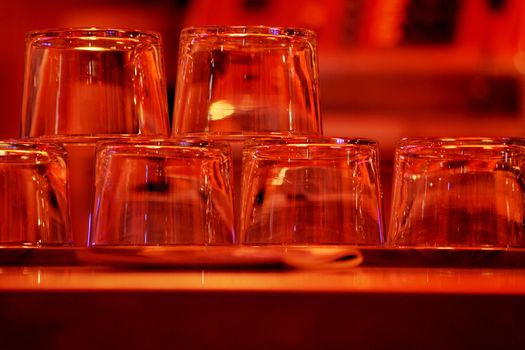 Color photo in red tones of a group of upturned clear wine glasses sparkling in the light in a pub / public house restaurant bar at night in Chueca in Madrid Spain. The multiple glasses have just been washed and dried, and are displayed stacked upside-down on the top of the bar where they are reflecting the light from above, ready to be filled with wine and served to the evening's customers. 