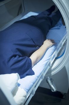 Female patient aged 45-55 wearing flower dress lying down in hyperbaric oxygen chamber receiving Hyperbaric Oxygen Therapy (HBOT) specialised medical treatment for injuries.