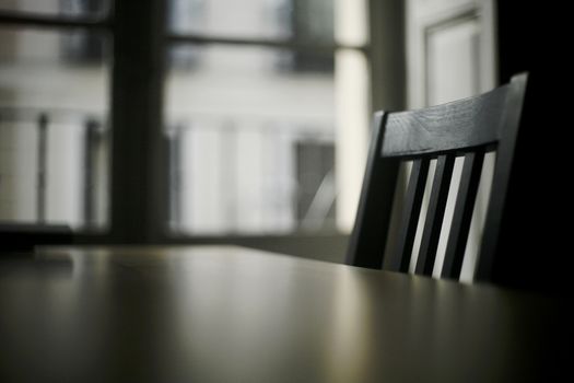 Table and black wooden chair in room with window in evening light and dark effect. 