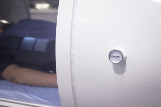 Female patient aged 45-55 wearing flower dress lying down in hyperbaric oxygen chamber receiving Hyperbaric Oxygen Therapy (HBOT) specialised medical treatment for injuries.