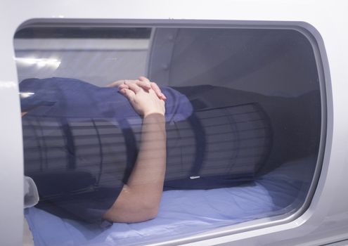 Female patient aged 45-55 wearing flower dress lying down in hyperbaric oxygen chamber receiving Hyperbaric Oxygen Therapy (HBOT) specialised medical treatment for injuries.