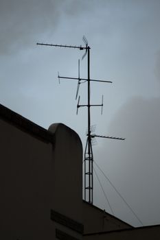 TV arial television antenna tied with metal cables onto roof of a building and blue grey sky in Madrid Spain. 