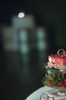 Candy bar heart shape and strawberry shape sweets trolley in wedding reception party with focus on foreground and negative space in grey defocused blur for publicity space. 