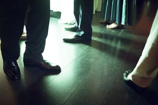 Legs of men and lady wearing standing on shiny tile floor in social event wedding marriage party in Madrid Spain. Green evening night tone color photograph. 