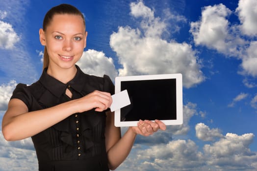 Beautiful businesswoman holding blank tablet PC and blank business card in front of PC screen. Blue sky and clouds as backdrop