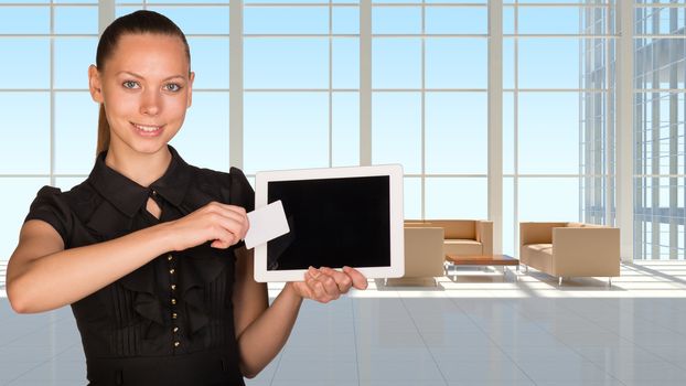 Beautiful businesswoman holding blank tablet PC and blank business card in front of PC screen.White roomy hall with sofas and coffee table as backdrop