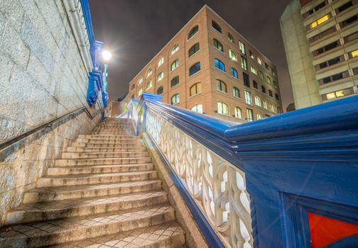 Stairs of Tower Bridge at night with surrounding buildings, London.
