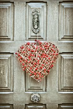 A heart shaped christmas wreath on a wooden front door