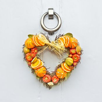 A heart shaped fruit christmas wreath on a wooden front door