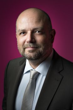 Pleasant businessman in dark suit and tie against magenta background