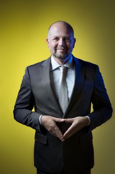 Businessman in dark suit makes with his hands diamond against yellow background