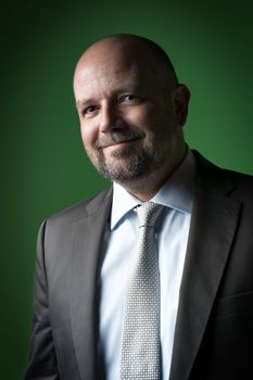 Image of a pleasant businessman with a bald head and beard against a green background