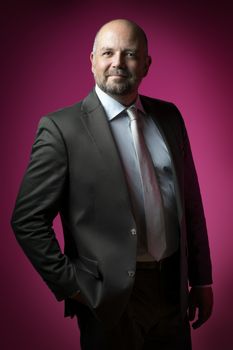 Friendly businessman in dark suit and tie against magenta background