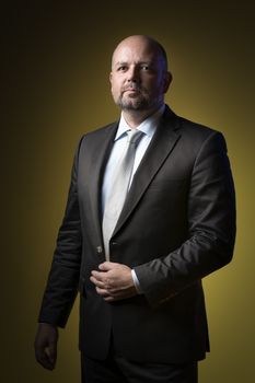 Serious businessman in dark suit and tie against yellow background