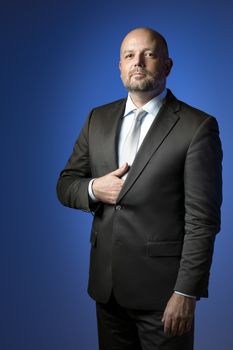 Serious businessman in dark suit and tie in front of blue background