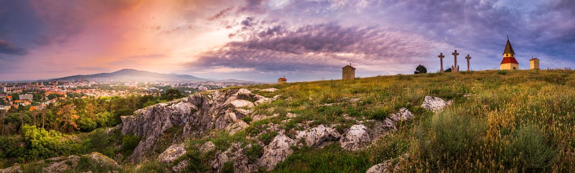 City and Village under a Hill at Sunset as Seen from Calvary, Nitra, Slovakia. Meadow with Flowers and Rocks in Foreground.