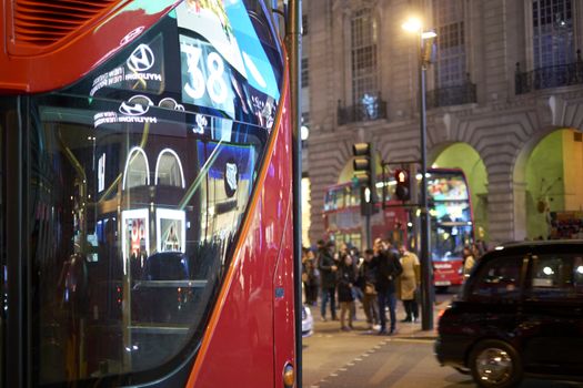 LONDON, UK - DECEMBER 19: Detail of London red bus line 38 reflecting lights of Piccadilly Circus at night, with busy street in the background. December 19, 2014 in London.