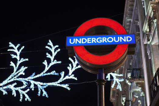 LONDON, UK - DECEMBER 20: Nighttime shot of London underground entrance sign with Christmas lights in the background. December 20, 2014 in London.
