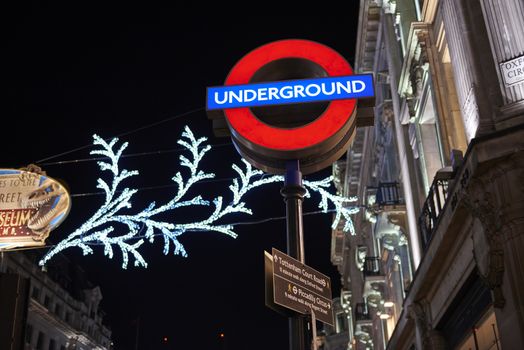 LONDON, UK - DECEMBER 20: Nighttime shot of London underground entrance sign with Christmas lights in the background. December 20, 2014 in London.