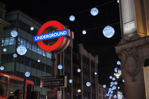 LONDON, UK - DECEMBER 20: Nighttime shot of London underground entrance sign with Christmas lights in the background. December 20, 2014 in London.