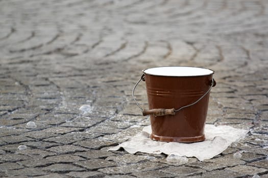 Photo shows a closeup of a water pail on the street.